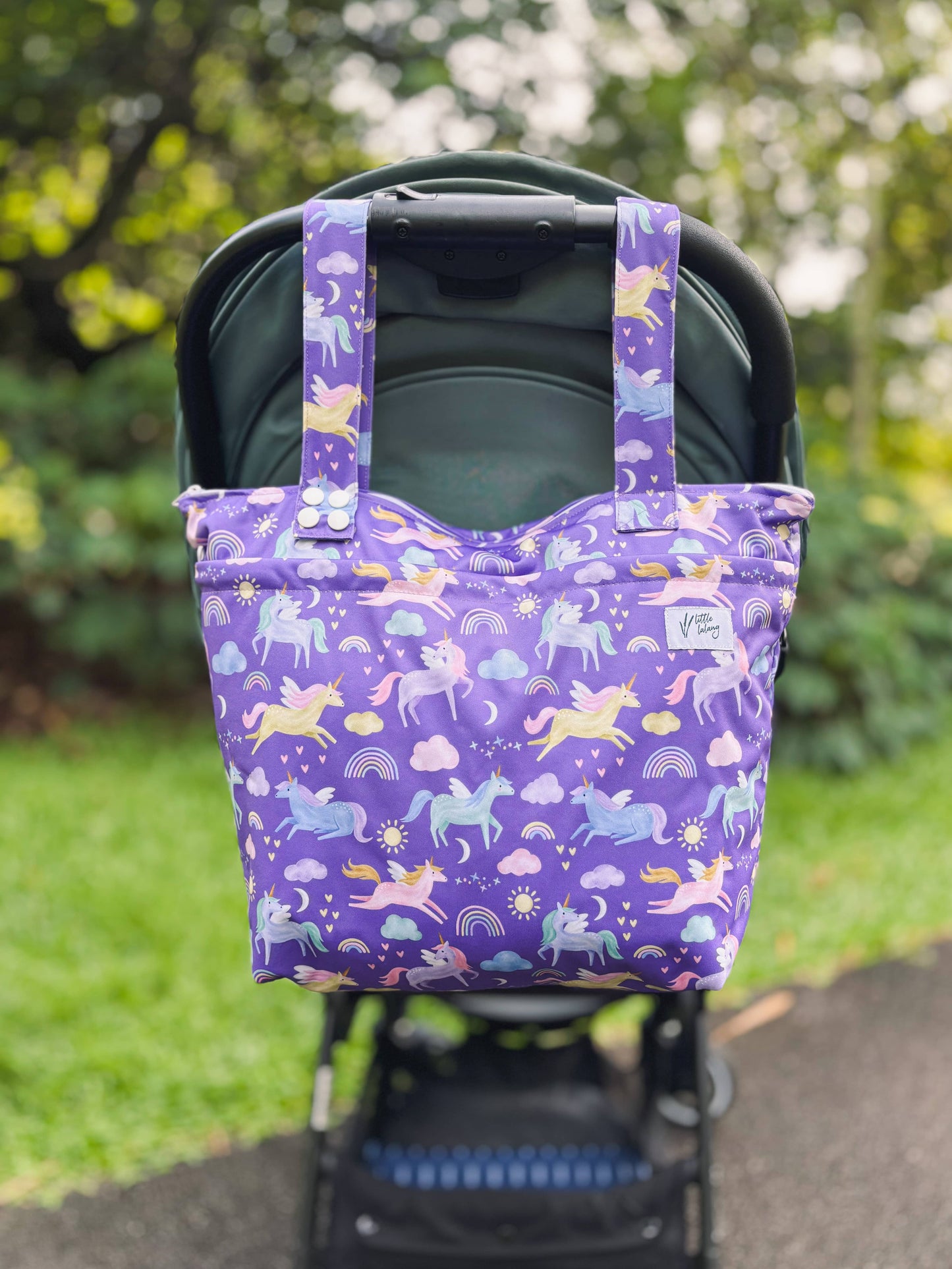 Purple tote bag with unicorn design attached to a stroller outdoors