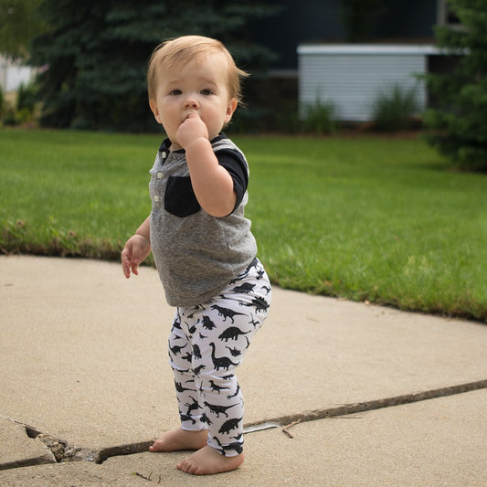 A toddler wearing black and white leggings with a dinosaur print standing on a sidewalk.
